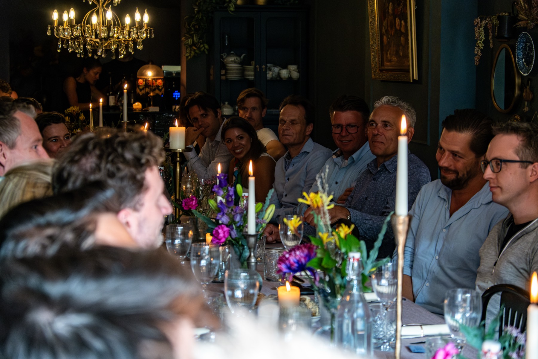 Guests at a long candlelit dinner table with flowers